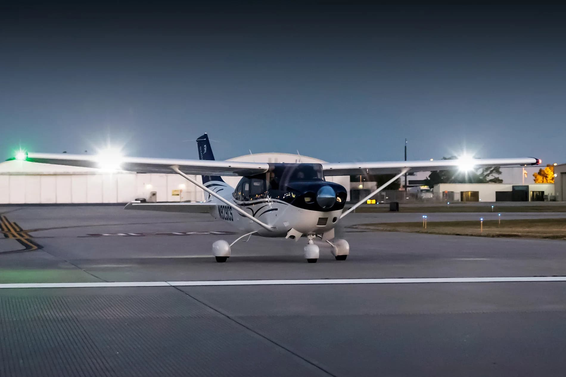 A Cessna Stationair on the tarmac at night with its lights on.