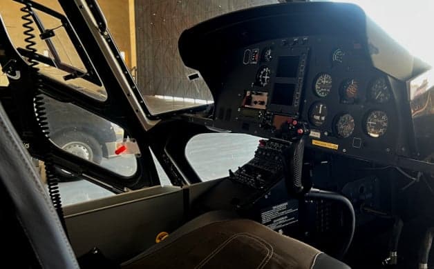 A dark blue helicopter is parked in a hangar with its doors open.