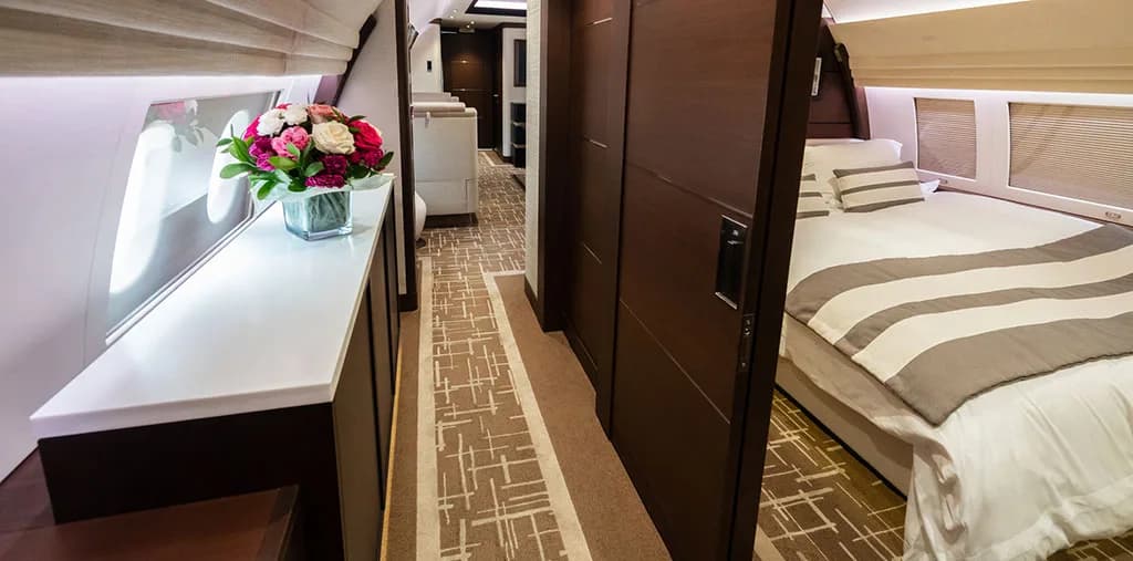 A view down a luxurious aircraft hallway with a fresh bouquet of flowers on a counter and a bedroom visible on the right.