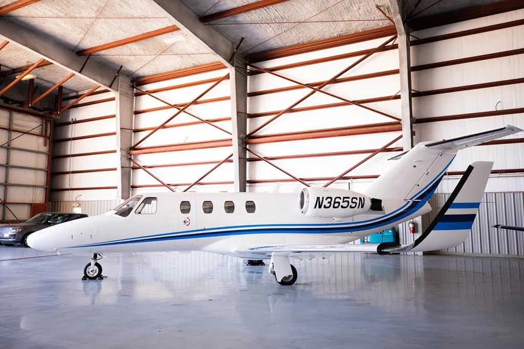 A white business jet with blue stripes, registration N365SN, parked inside a hangar.