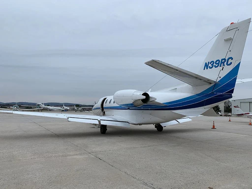 Rear view of a white business jet with blue stripes and registration N39RC parked on an airfield.