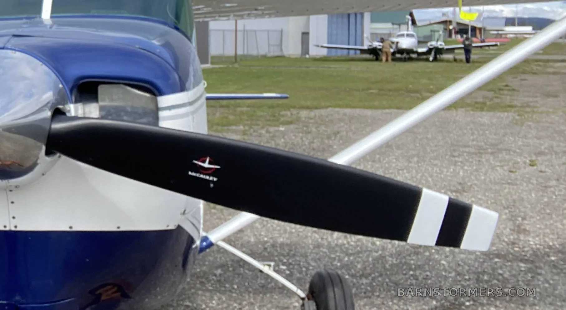 A close-up view of a blue and white aircraft's propeller and nose, with other planes in the background.