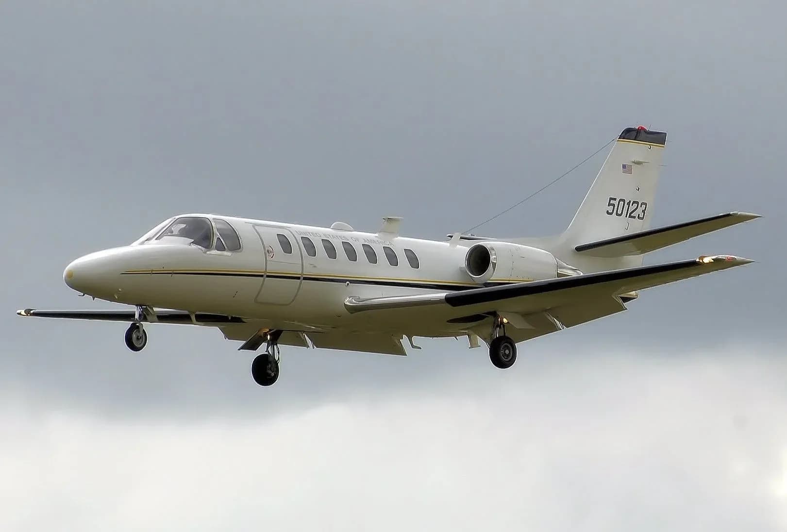A white Cessna Citation CJ1 with registration 50123 is shown in flight against a cloudy sky.