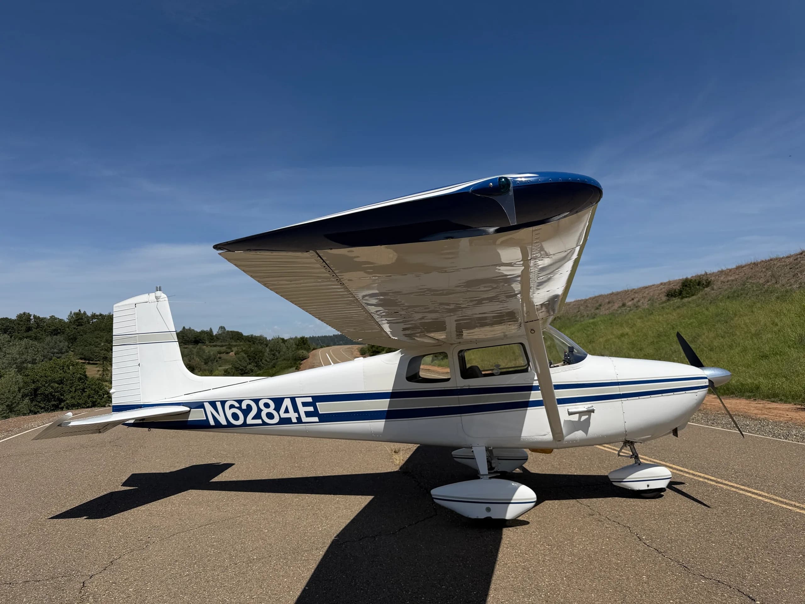 A white Cessna 172 with blue stripes, registration N6284E, parked on an asphalt surface under a clear blue sky.