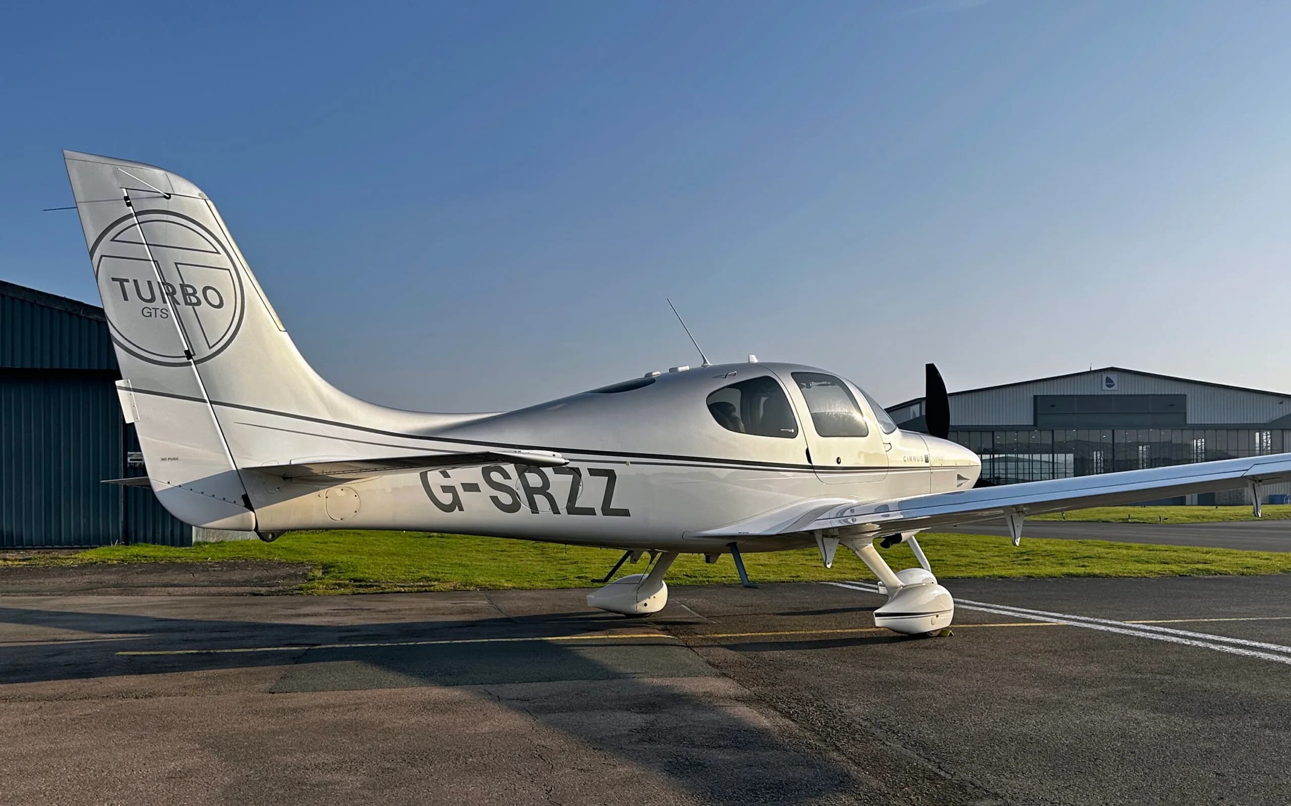 A silver and white Cirrus SR22 Turbo aircraft with registration G-SRZZ parked on an airfield.