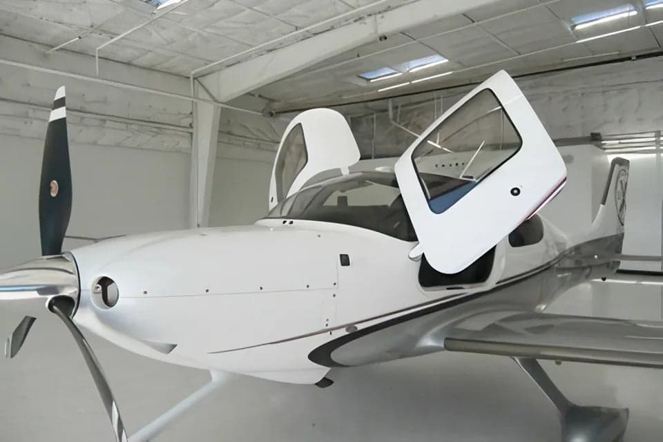 A Cirrus aircraft is parked in a hangar with its gull-wing doors open.
