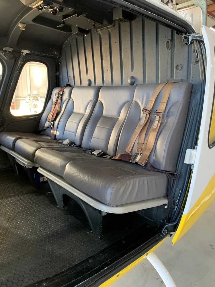 The interior of the helicopter cabin features three grey leather passenger seats with brown harnesses.