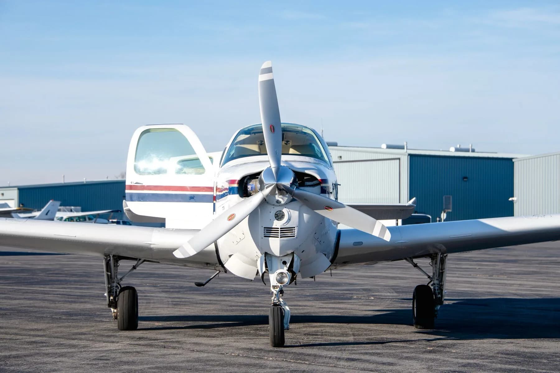 Front view of a white Beechcraft Bonanza N2261L with the pilot's door open on an airfield.