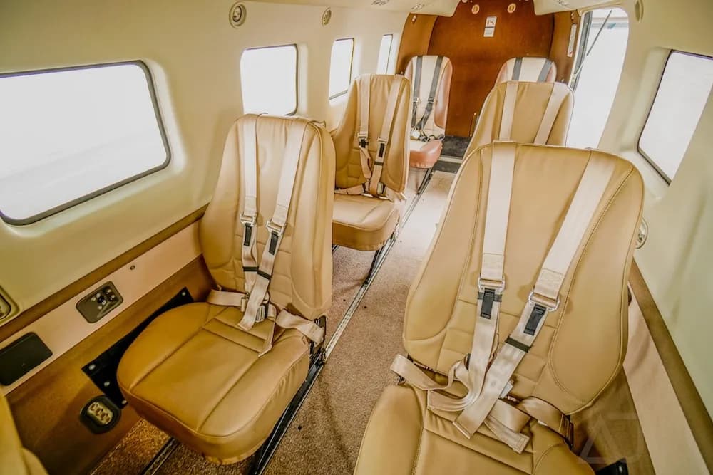A side view of the aircraft interior cabin, featuring tan seats with shoulder harnesses.