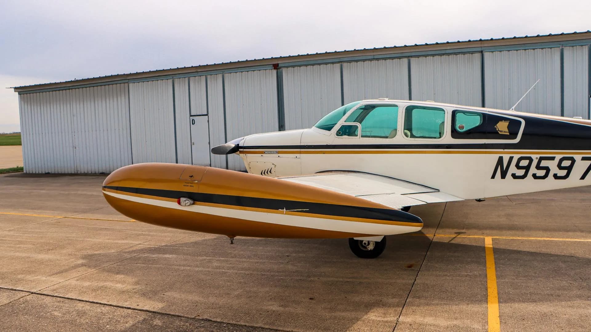 Side view of the front fuselage and wing of a white and gold Beechcraft Bonanza N9597R.