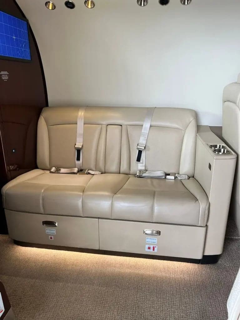 A tan leather bench seat with seatbelts and storage underneath in the aircraft cabin.