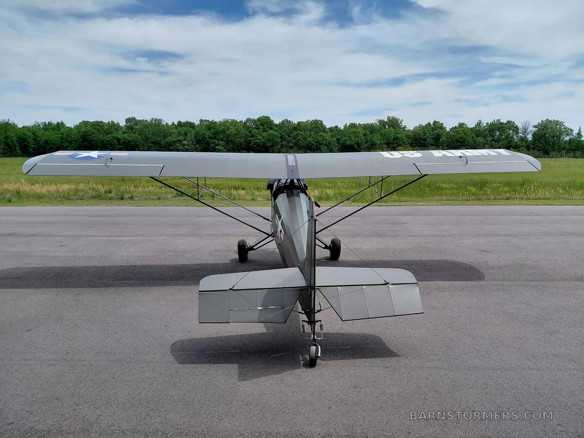 A dark green single-engine, high-wing aircraft with "US ARMY" written on the underside of its wing, viewed from the rear on an airfield.