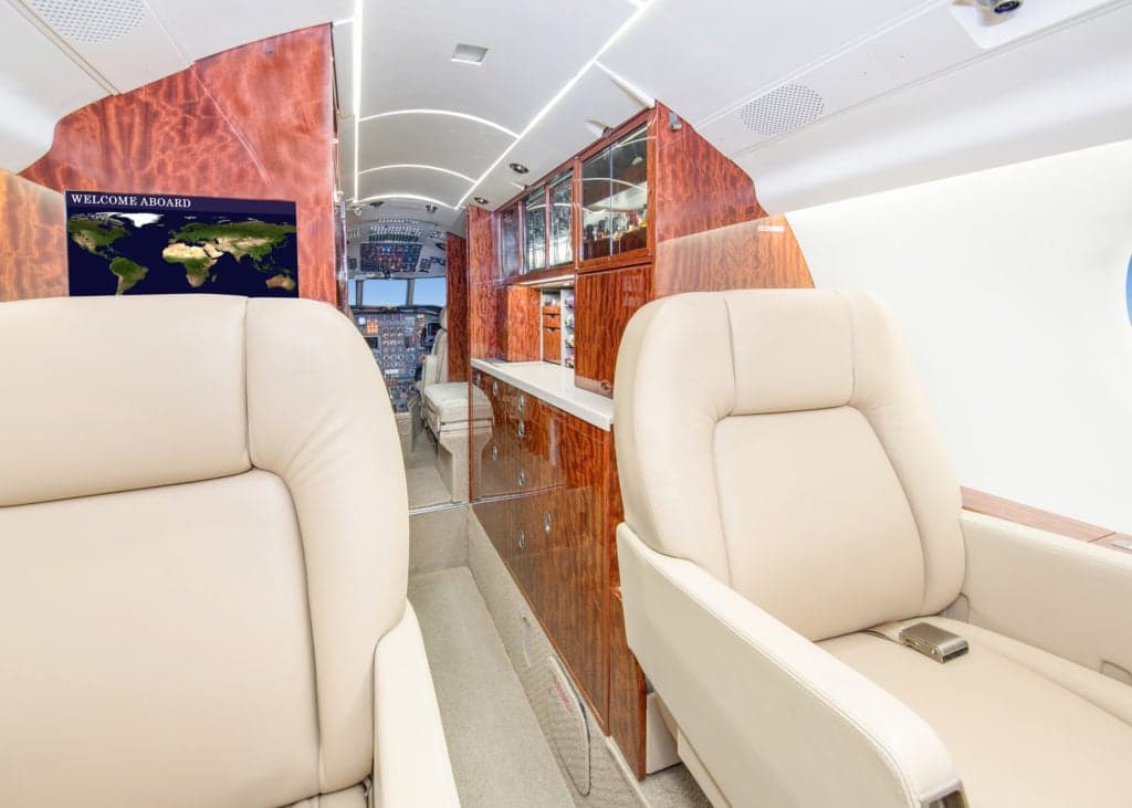 View of the interior cabin with cream-colored leather seats and wood trim.