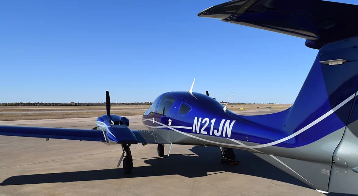 Rear quarter view of a Diamond DA62 aircraft with a blue and silver paint scheme, showing the registration N21JN.