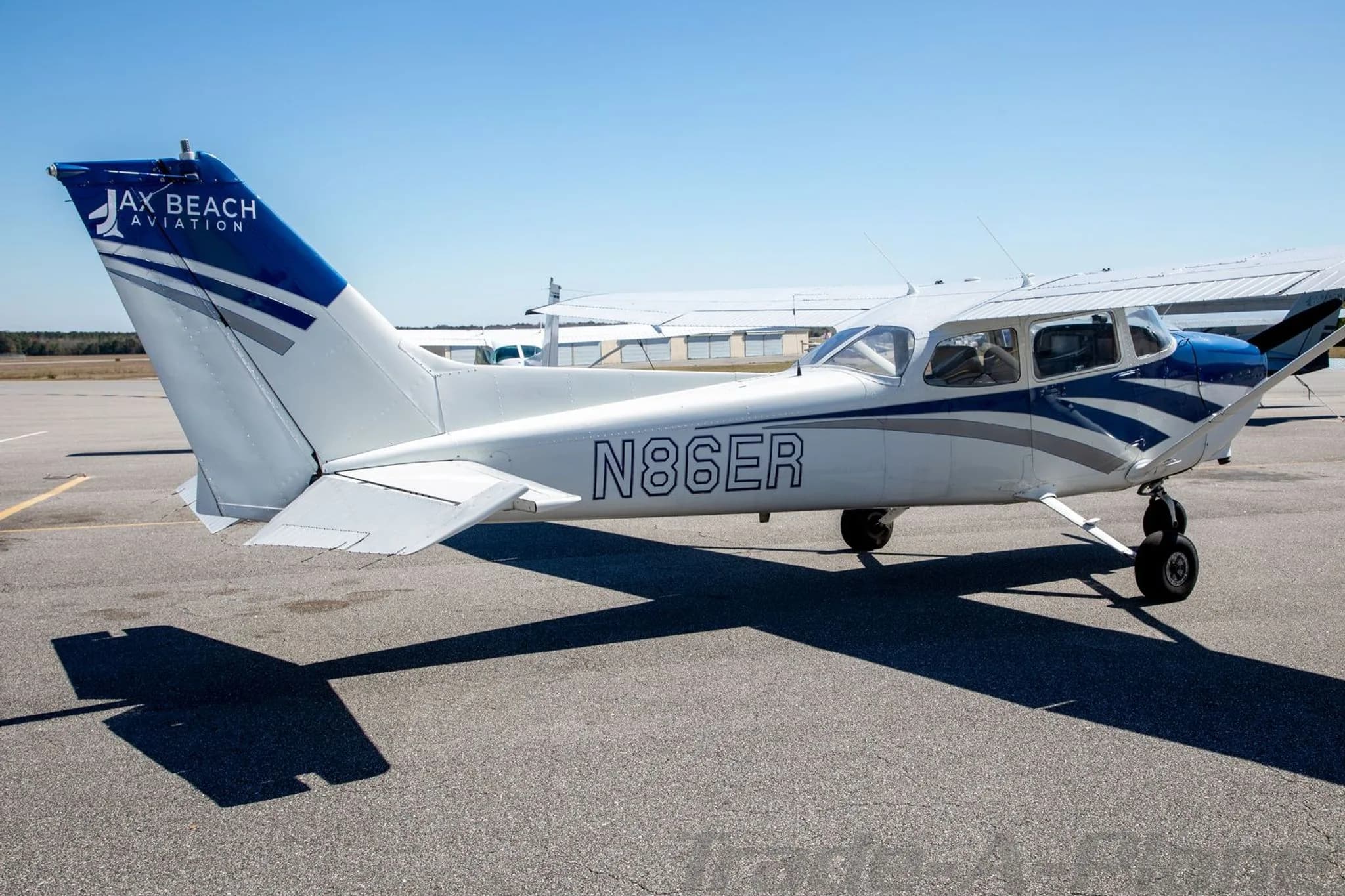 The rear-right view of the N86ER aircraft, a white and blue Cessna 172, parked on an airfield with 'JAX BEACH AVIATION' on the tail.