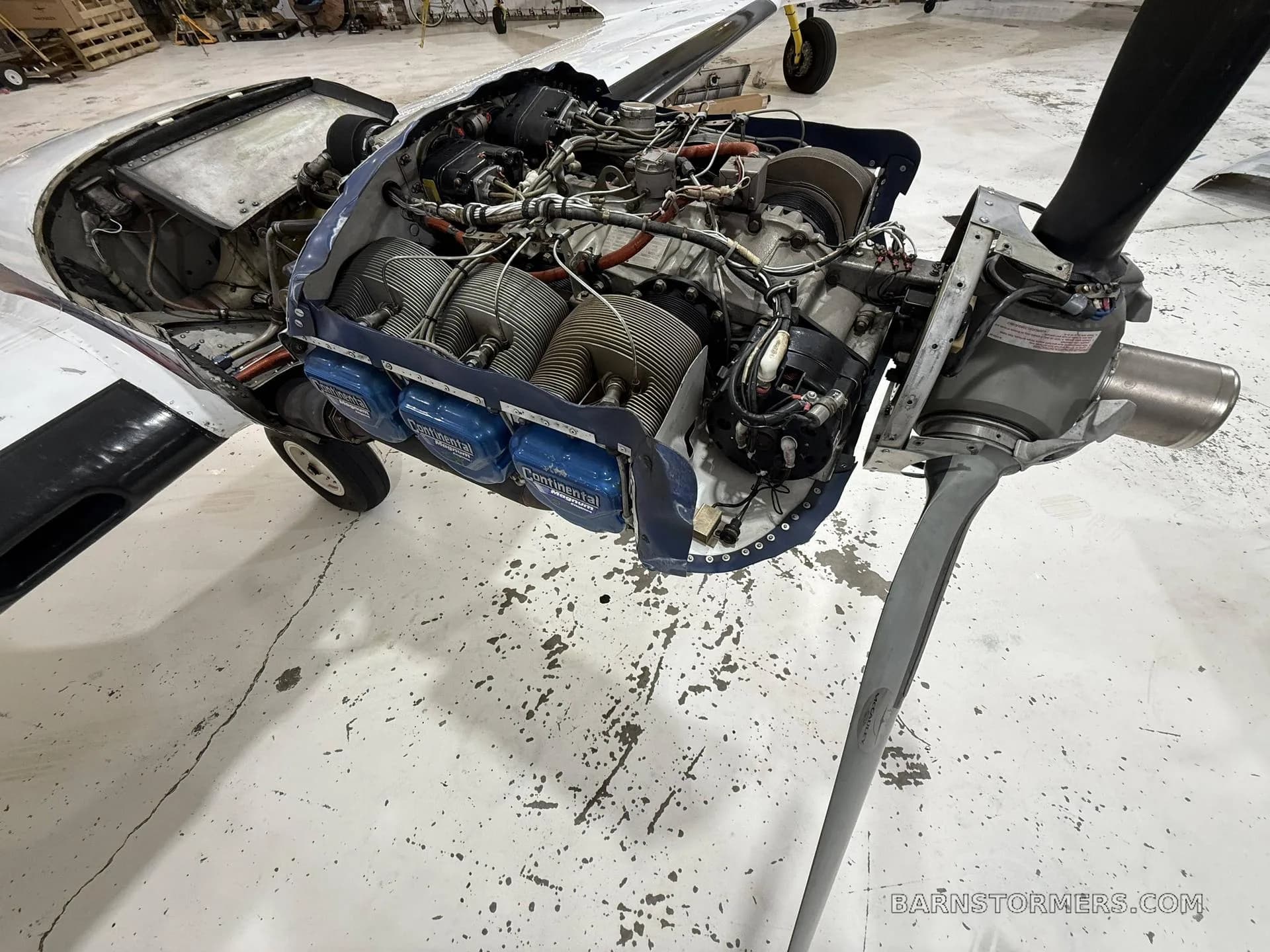 A close-up view of a Continental aircraft engine with its cowling removed, showing cylinders and wiring, in a hangar.