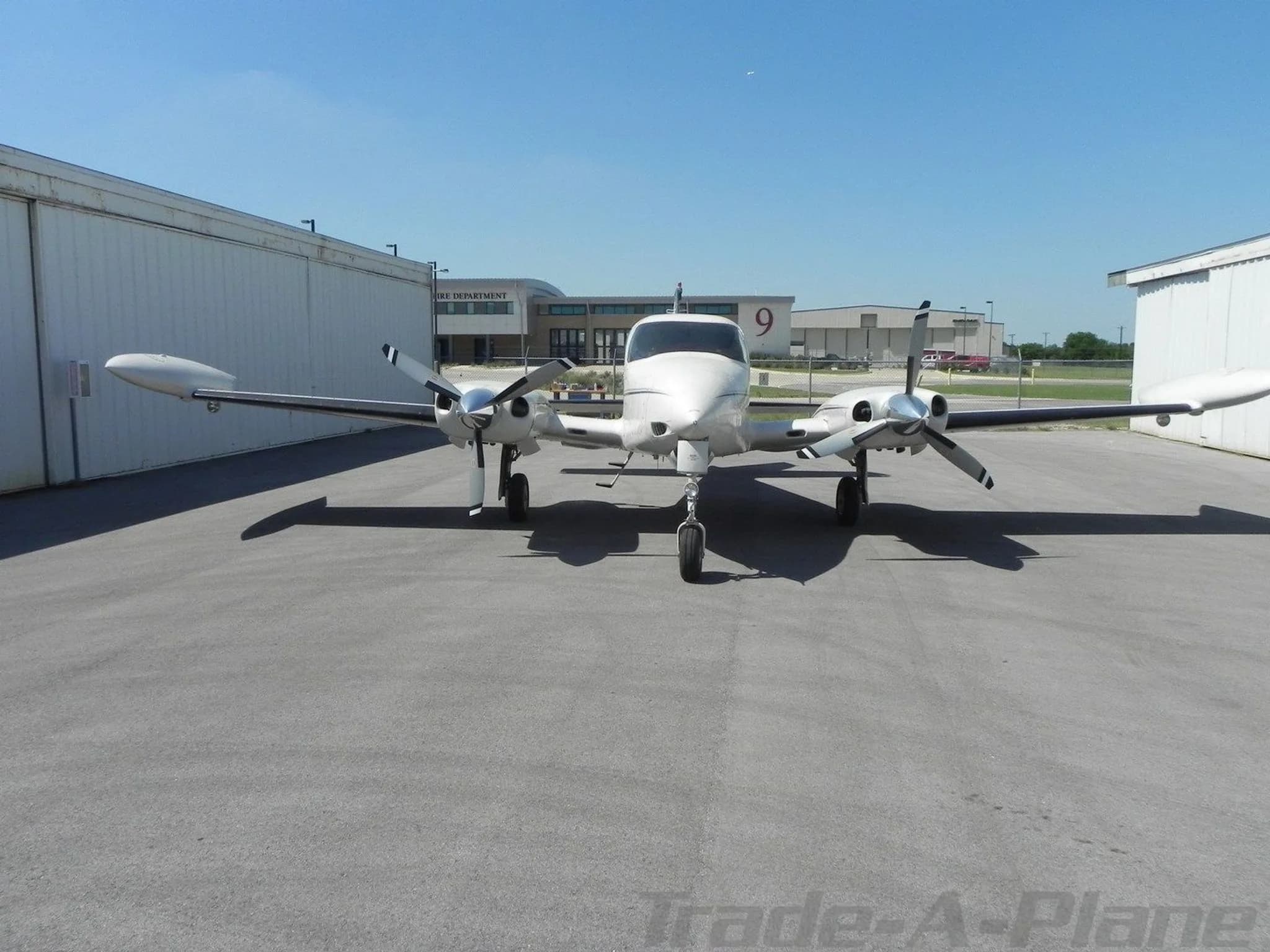 A front view of a white twin-engine Cessna 310 aircraft parked on an asphalt apron under a clear blue sky.