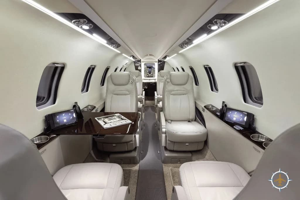 The luxurious interior of a business jet cabin with light-colored leather seats and dark wood tables.