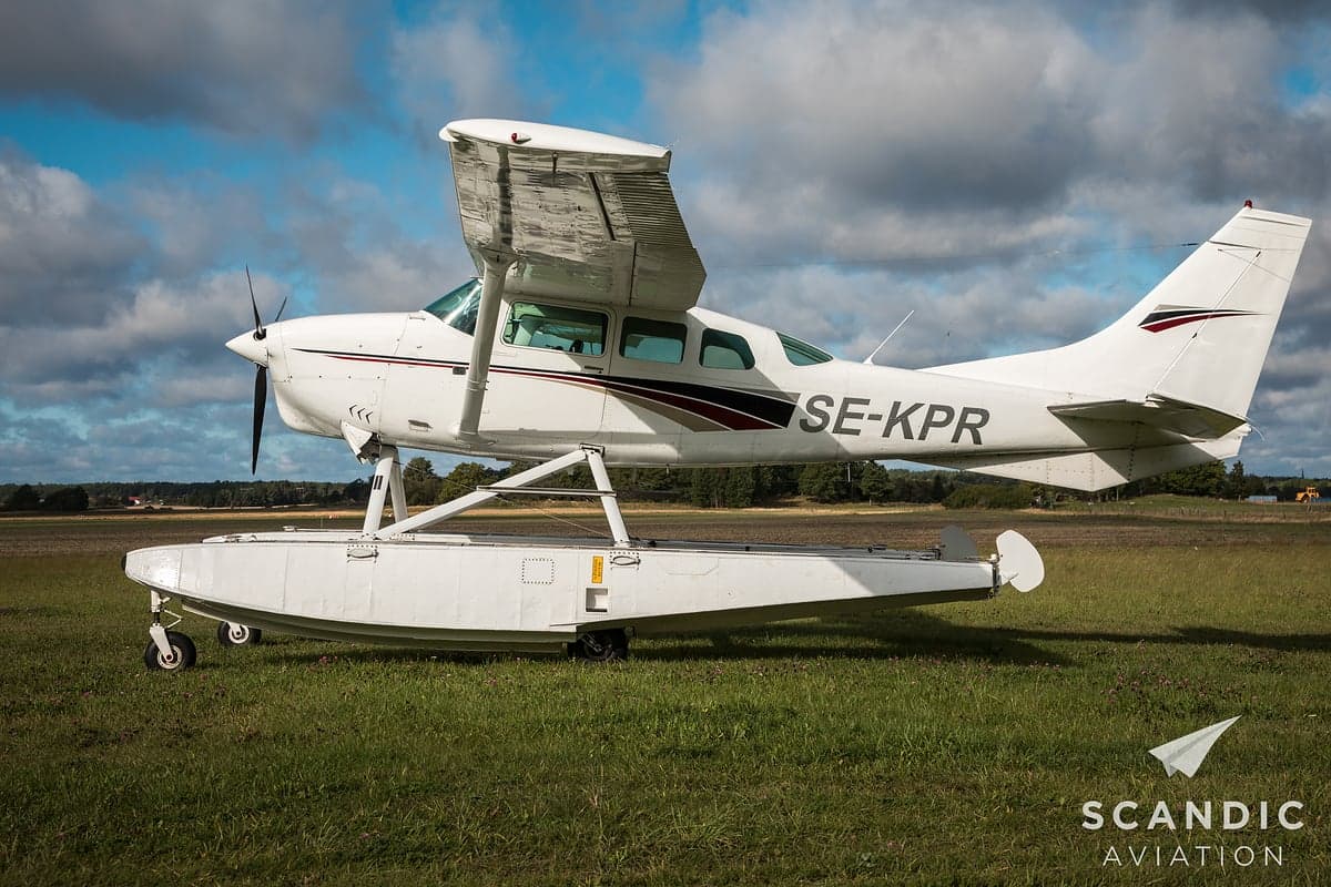 White and maroon floatplane parked on a grassy field.