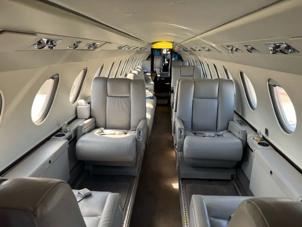 View down the aisle of a business jet cabin with light gray leather seats, looking towards the rear.