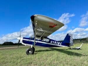 A blue and white ACA aircraft, registration N101BC, parked on a grassy field under a blue sky.
