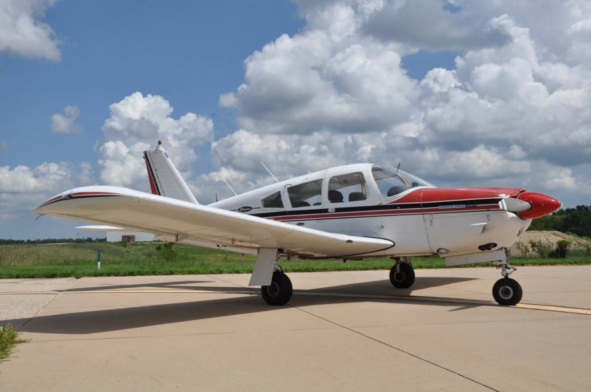 A Piper PA-28 Cherokee is parked on the tarmac on a sunny day.