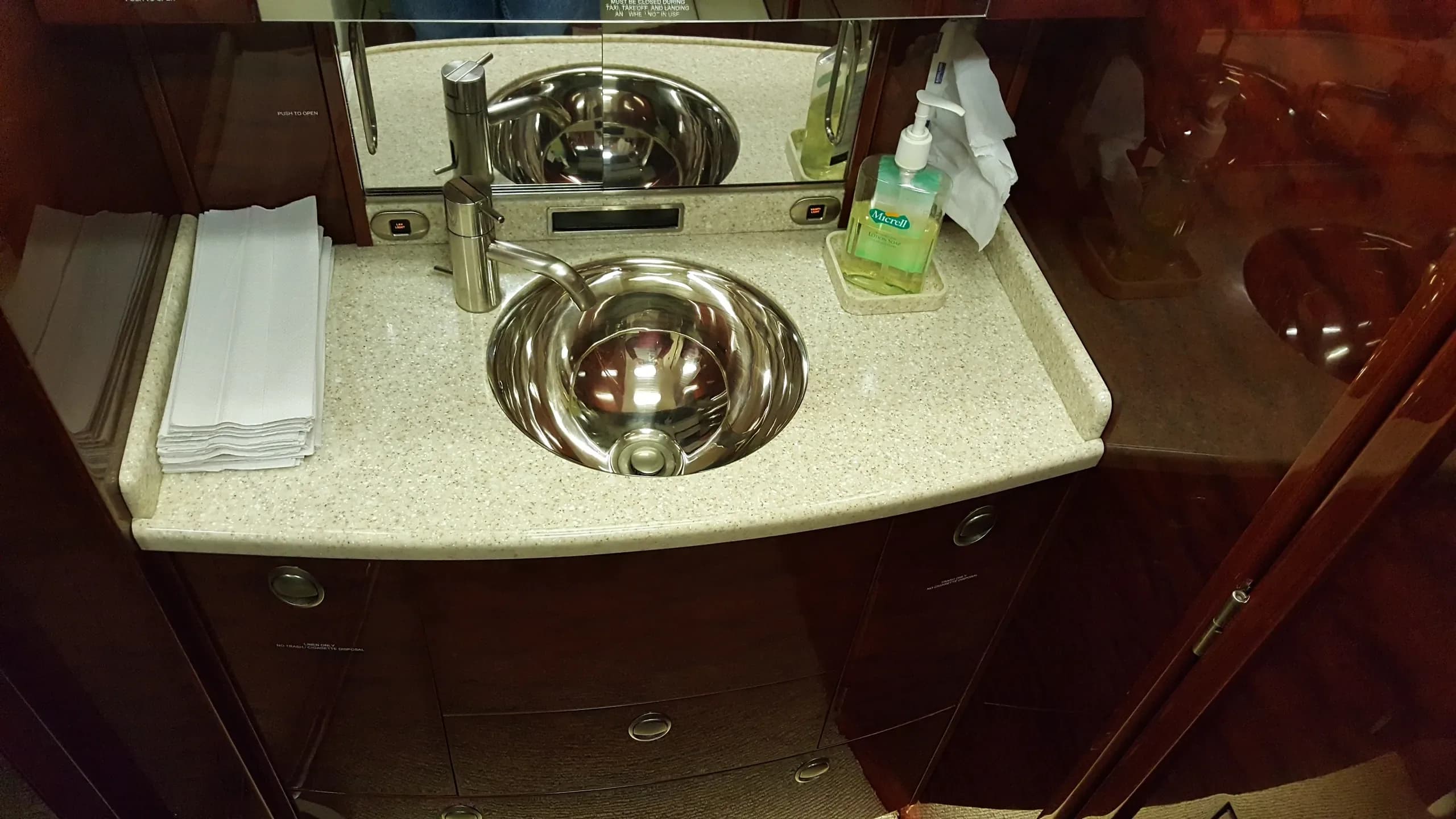 A private jet lavatory with a polished chrome sink, granite countertop, and dark wood cabinetry.