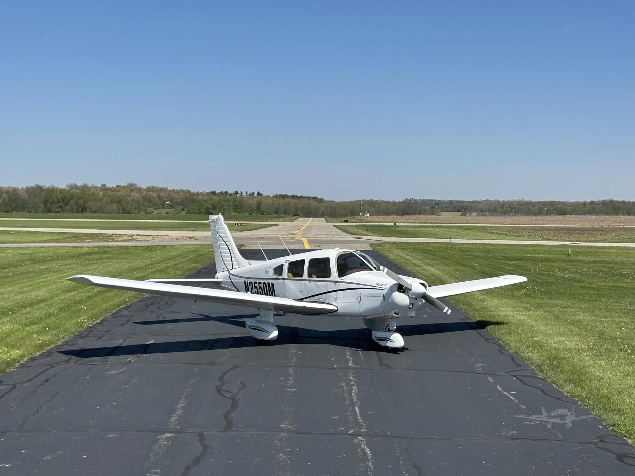 A white Piper Cherokee aircraft, N2550M, with black accent stripes, parked on an asphalt runway with green grass.