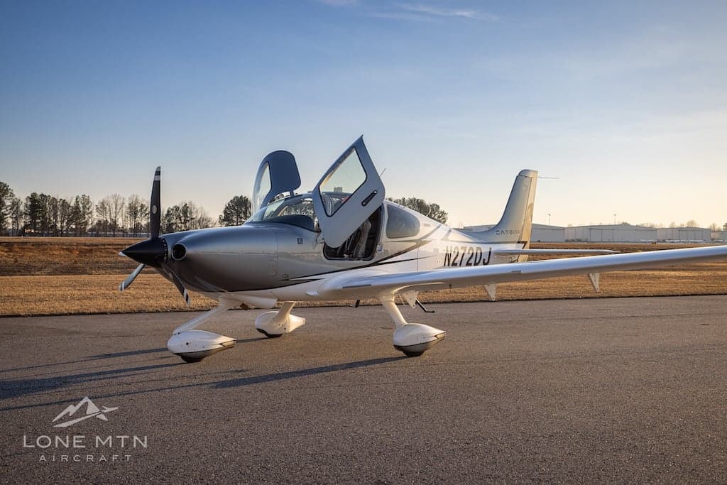 A Cirrus SR22T aircraft with open doors is parked on the tarmac at sunset.