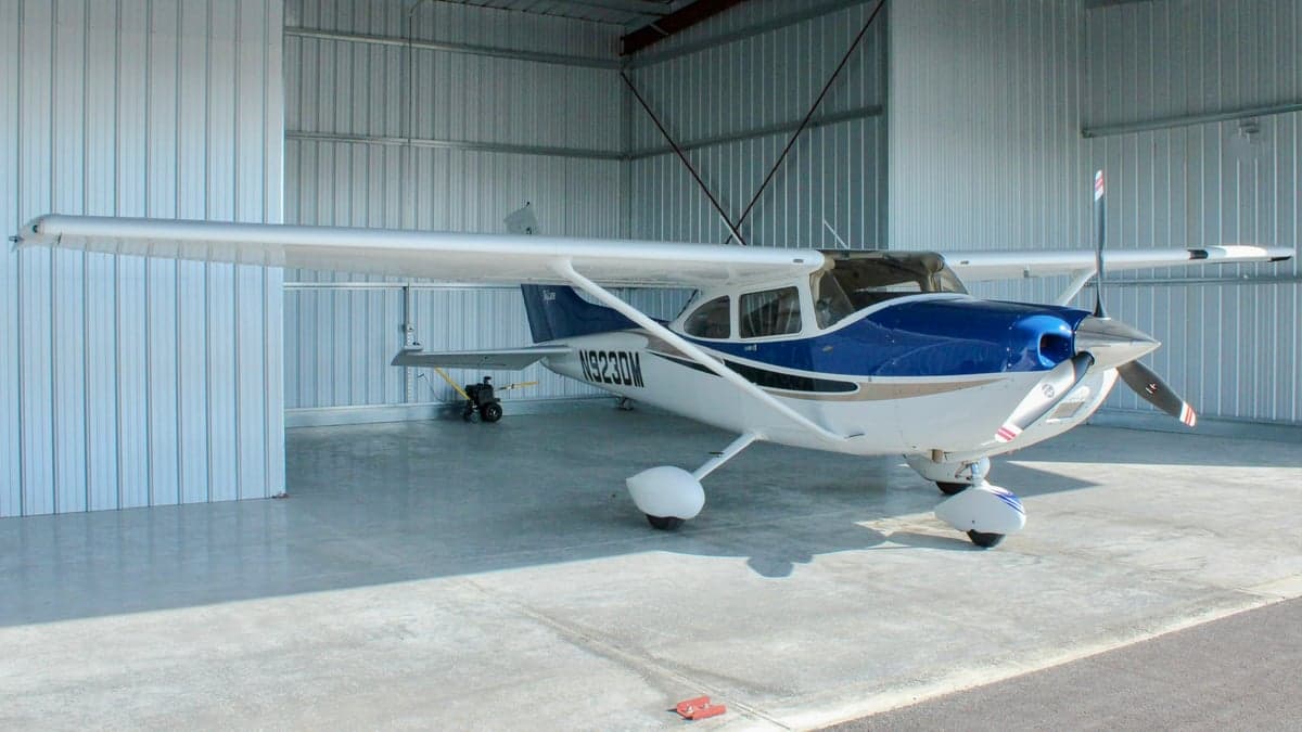 A white and blue single-engine propeller aircraft, N923DM, parked partially outside a metal hangar, viewed from the front-right.