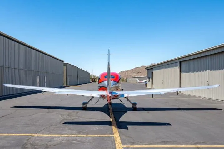 Rear view of a red and silver Cirrus SR22T aircraft (N566TT) parked between hangars.