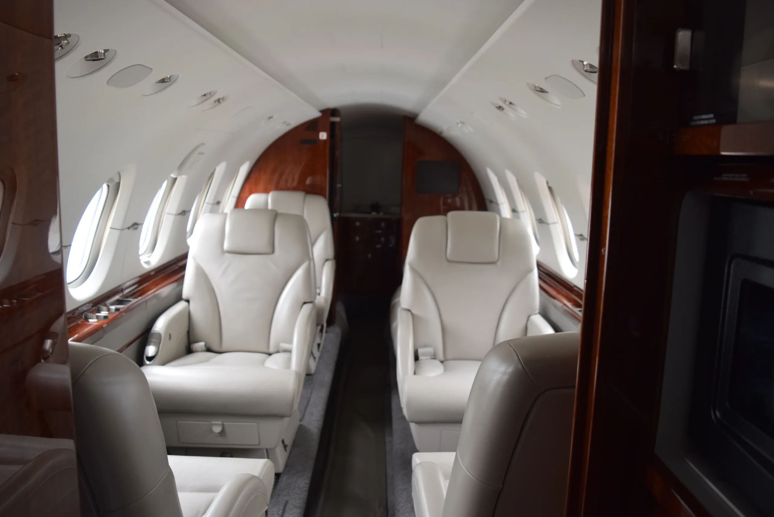 View of the aircraft cabin with cream-colored leather seats and wood trim.