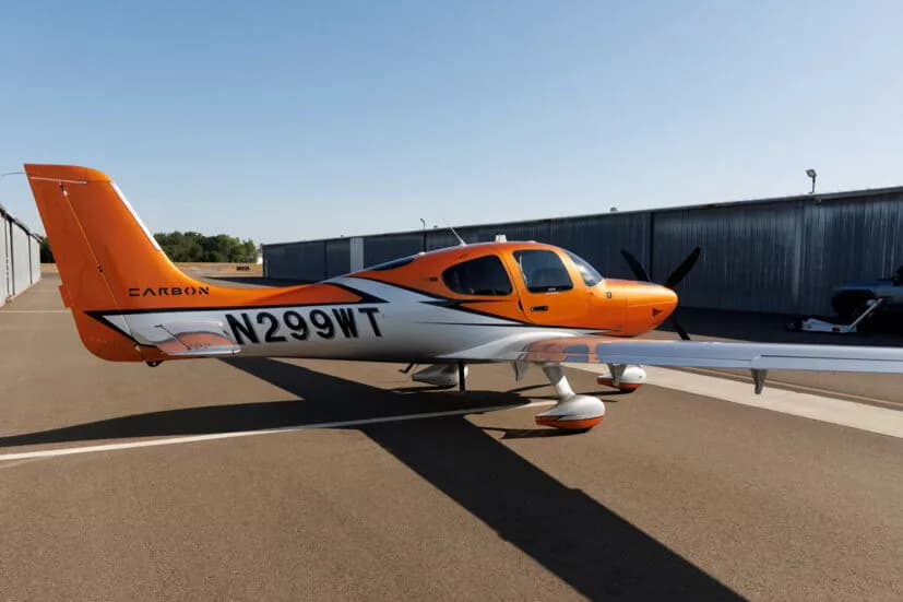 Side view of an orange and silver Cirrus SR22T GTS aircraft with registration N299WT parked on an tarmac.