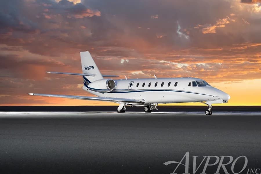 A side view of the white Cessna Citation Sovereign (N680FD) with blue and grey stripes, parked on a tarmac against a dramatic sunset sky.