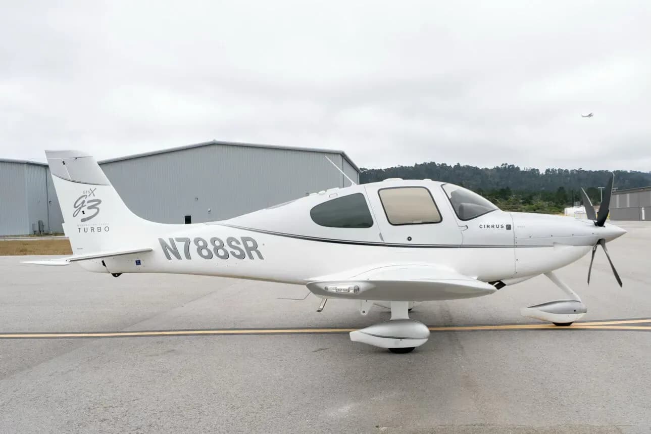 A white and grey Cirrus SR22 G3 Turbo aircraft, N788SR, parked on an airfield with hangars in the background.