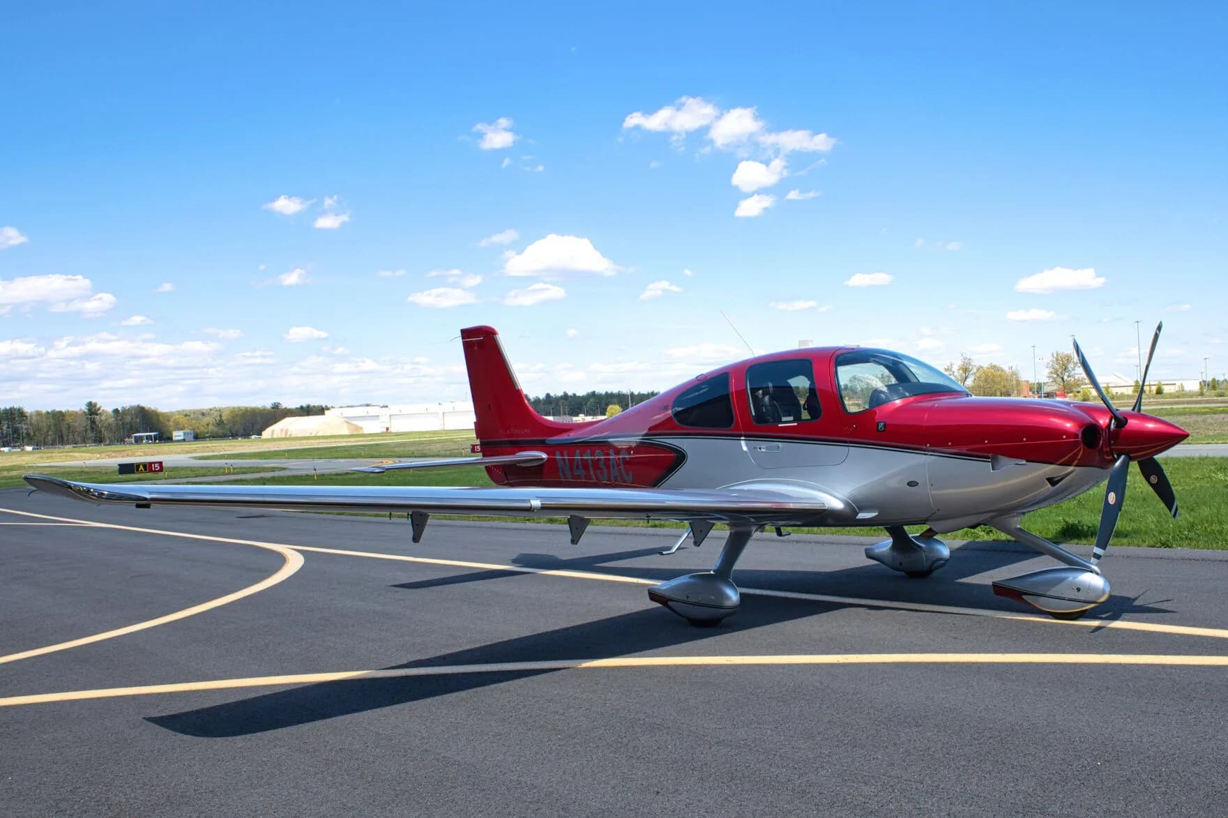 A red and silver Cirrus SR22T aircraft, N413AC, parked on an airport tarmac with a distant building.