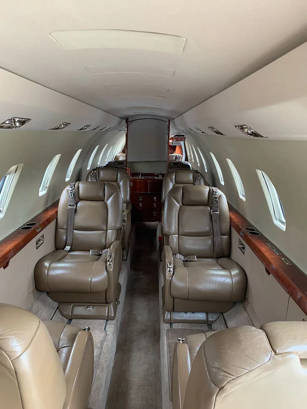 View down the aisle of the aircraft cabin, showing tan leather seats and wood trim.