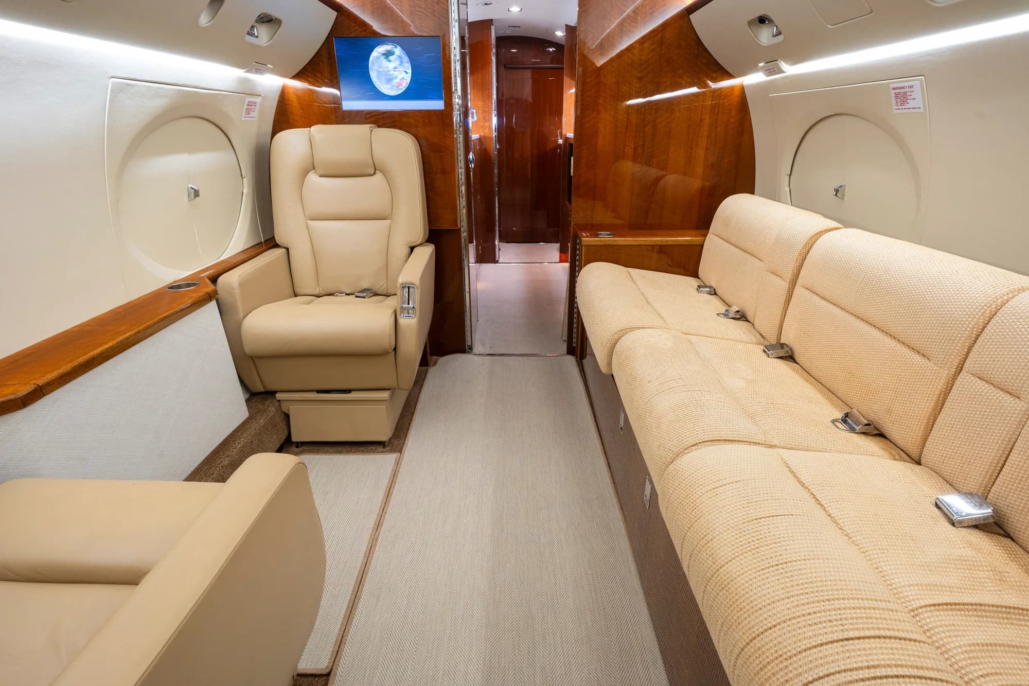 The aft section of a private jet cabin with a beige leather sofa and individual seats.