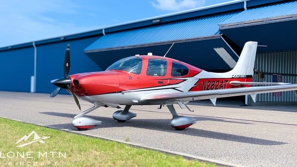 A red and silver Cirrus SR22T aircraft, registration N282AT, parked on an tarmac in front of a blue hangar.