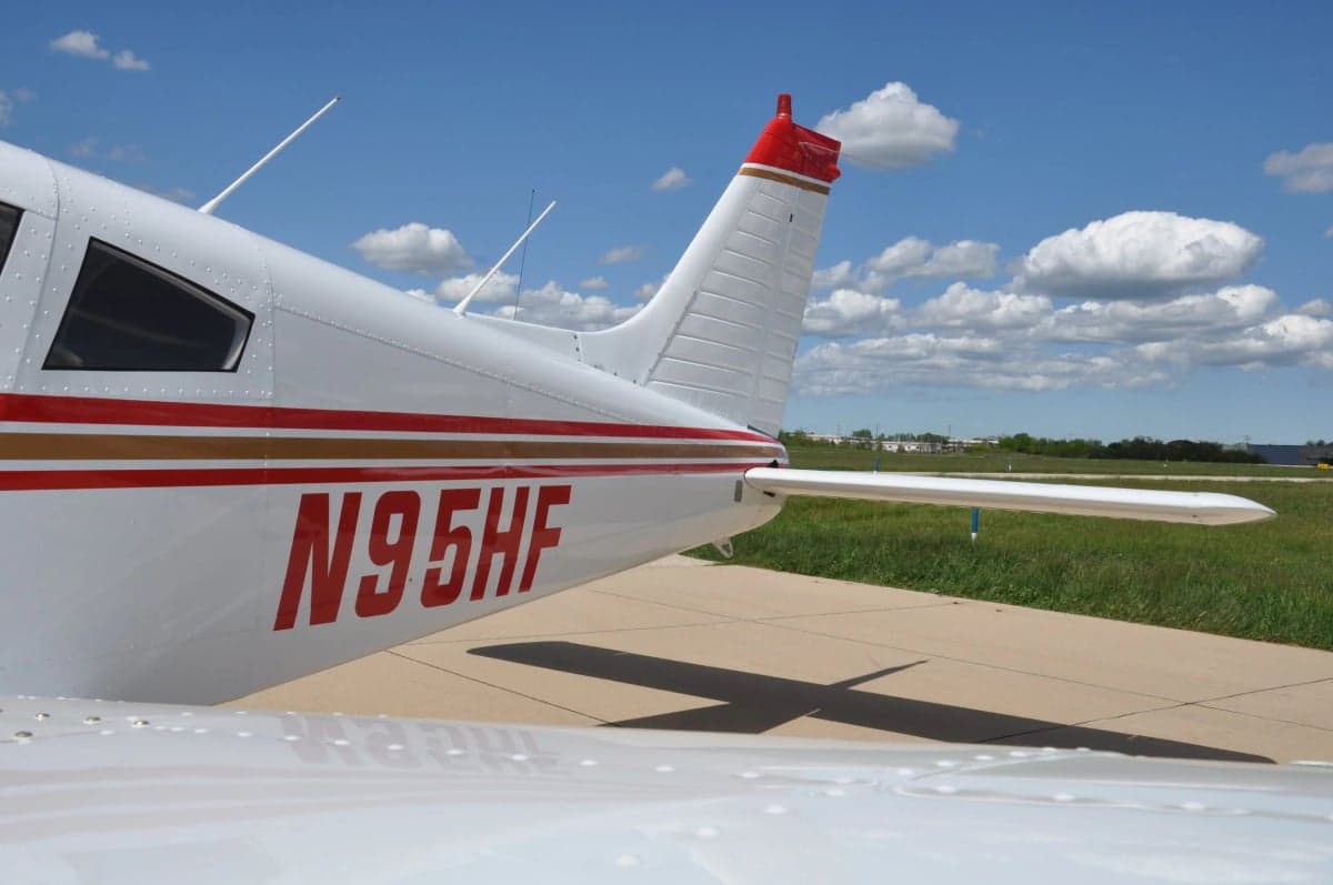 A close-up of the tail section of the white aircraft, featuring red and gold stripes and registration N95HF.