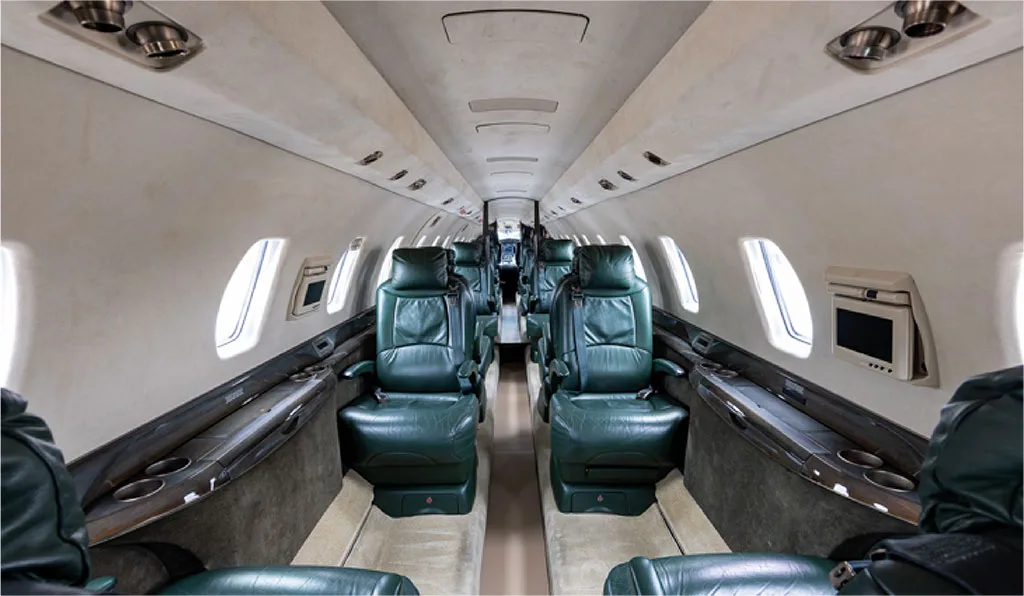 The interior cabin of a private jet with dark green leather seats and light-colored walls.