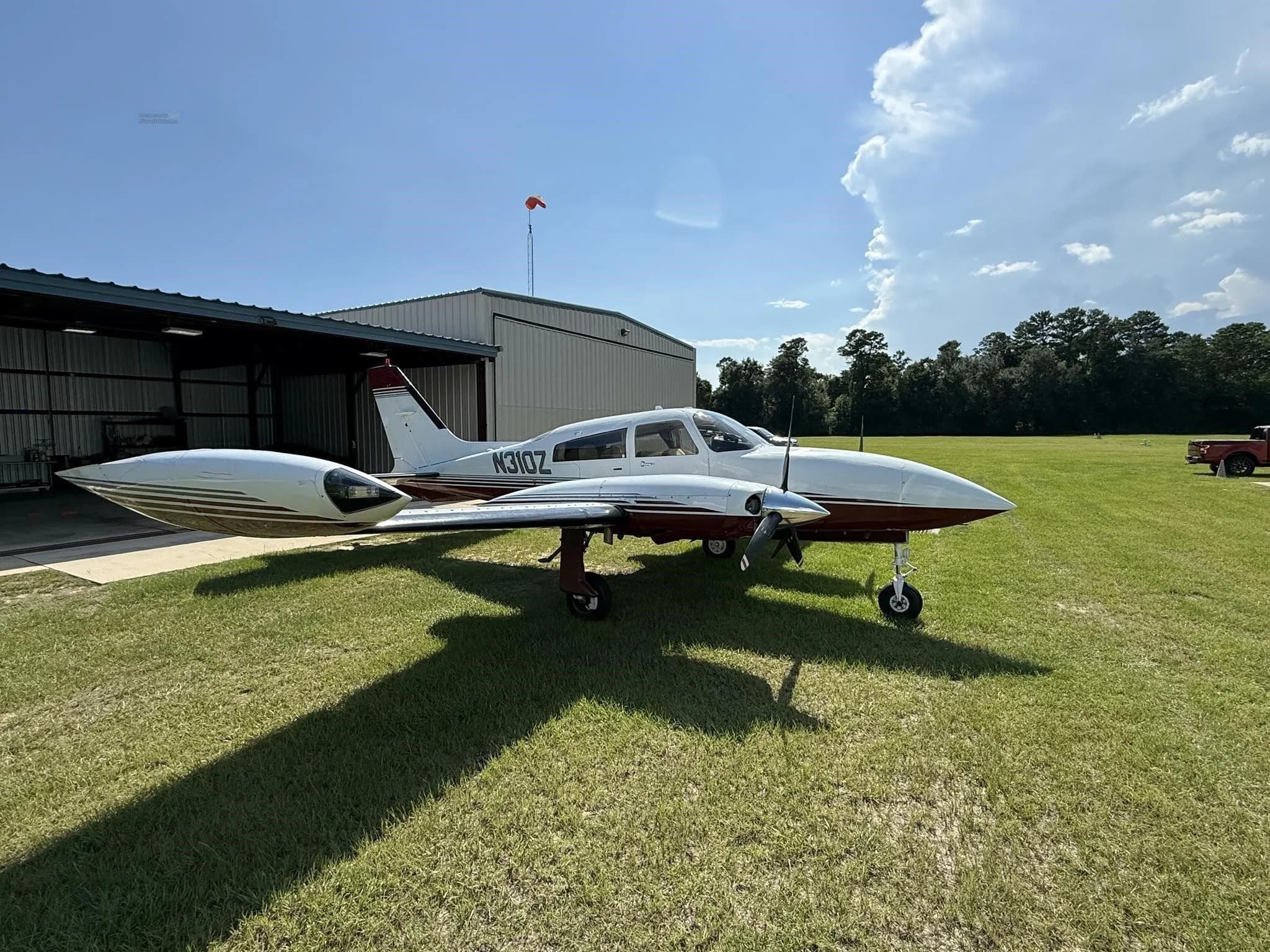 Side-right view of a white and red twin-engine aircraft (N310Z) parked on grass with a truck in the background.
