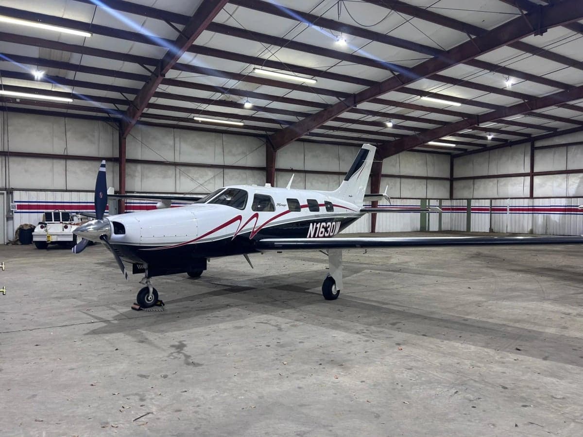 Side view of a Piper Mirage aircraft with a white and black paint scheme inside a hangar.