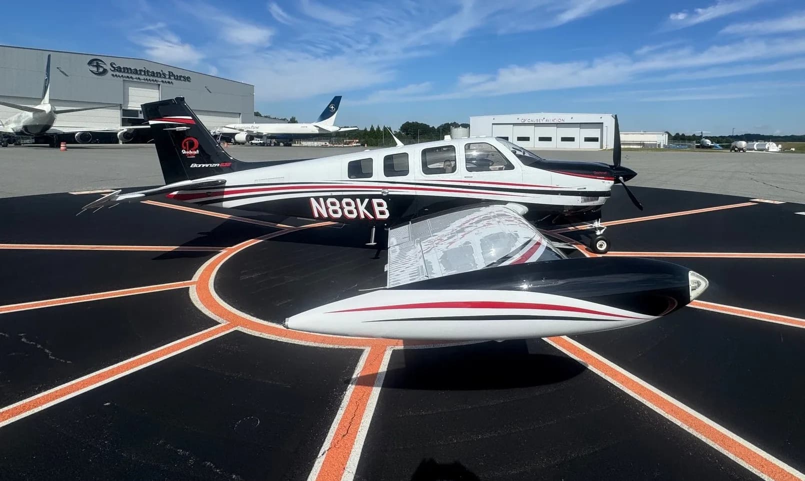 A three-quarter view of a white and black Beechcraft Bonanza with red stripes, tail number N88KB, on an airport tarmac.