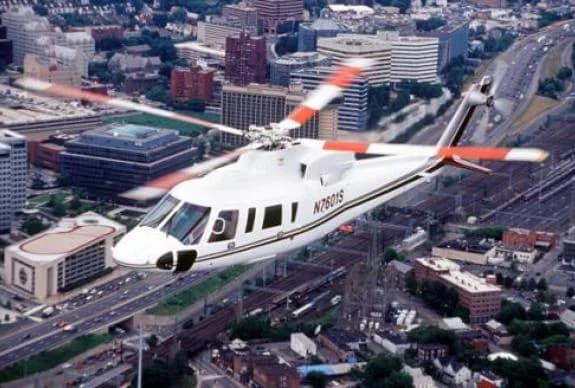 A white Sikorsky S-76 helicopter flying over a city.