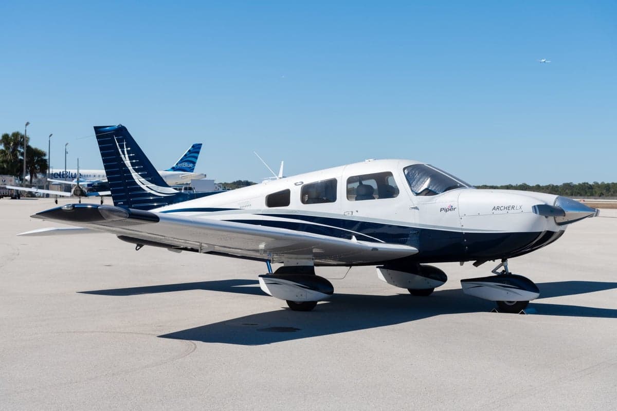 Side view of the Piper Archer LX N603CE on the tarmac with a JetBlue aircraft in the background.