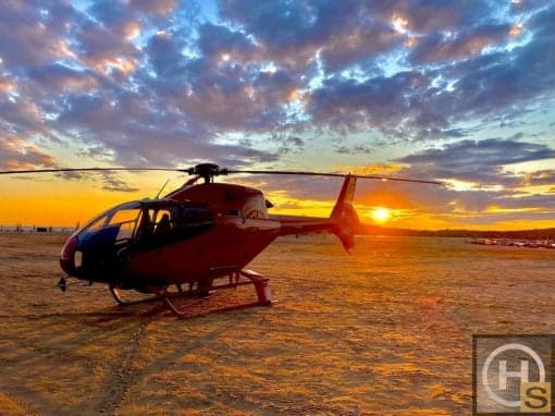 A red helicopter sits on the ground at sunset.