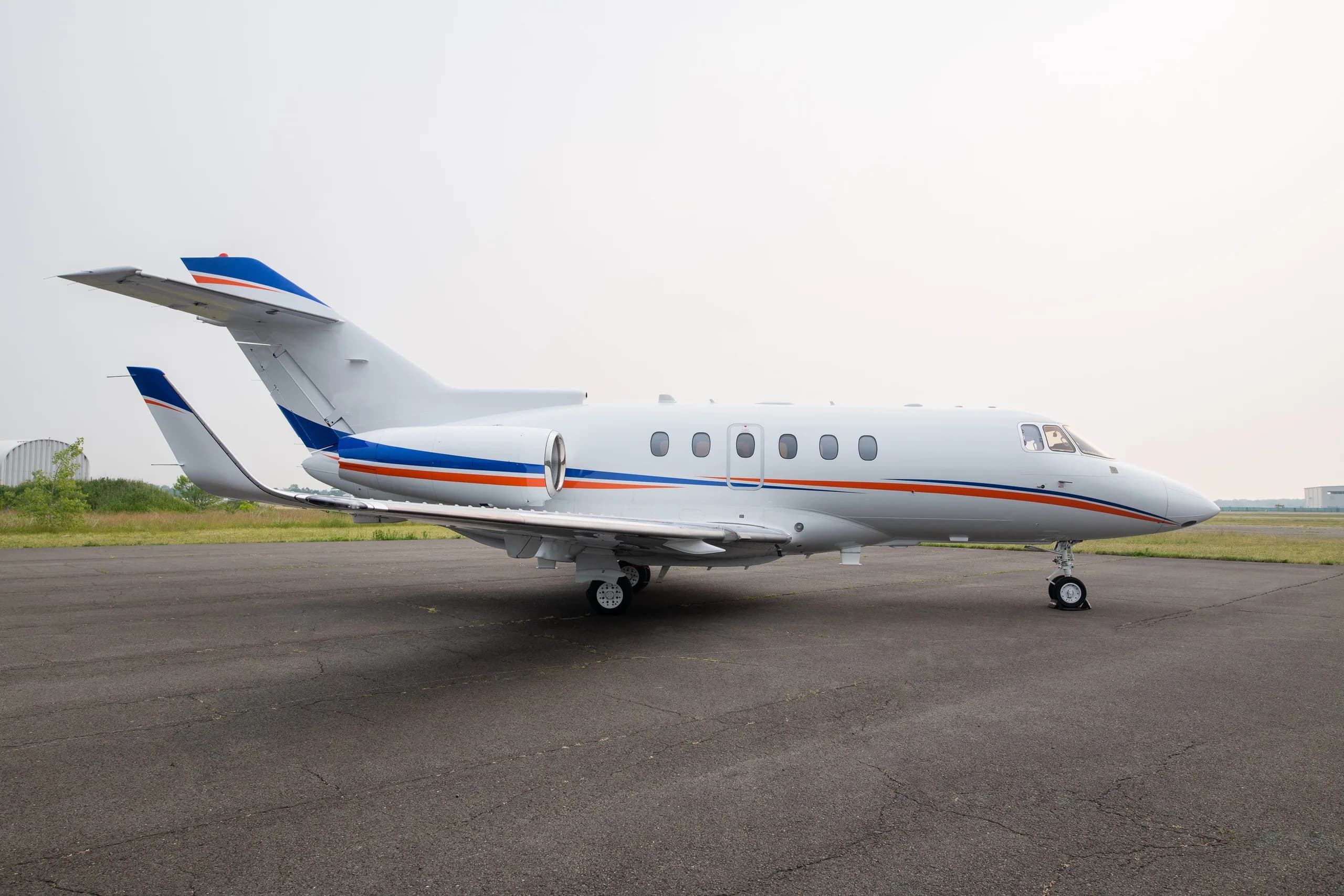 A white business jet with blue and orange stripes on the tarmac, viewed from the side.