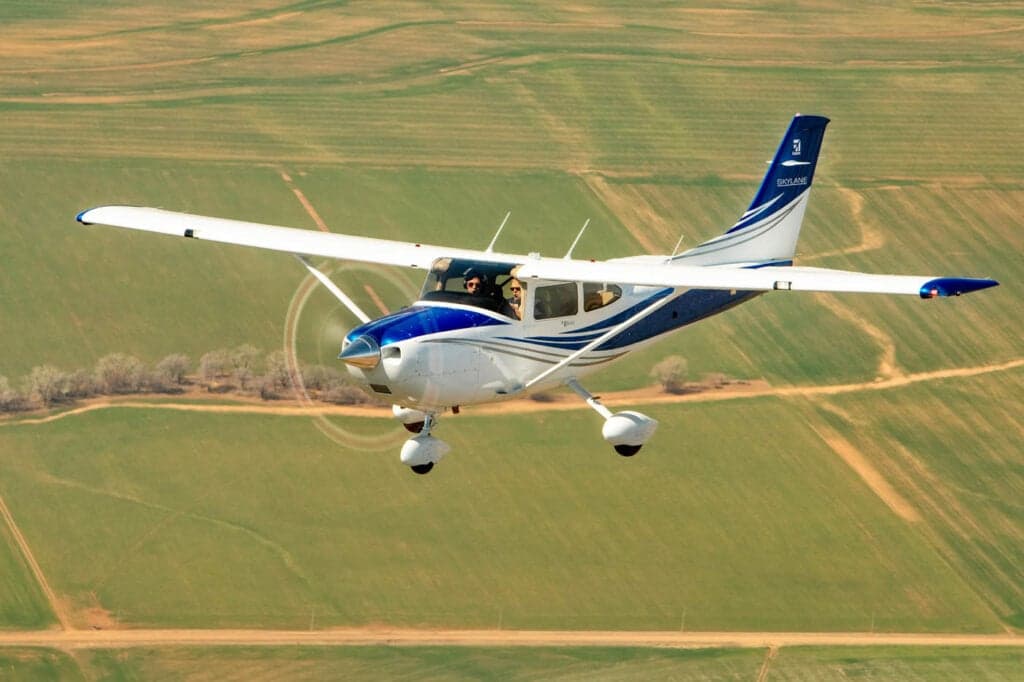 A Cessna Skylane in flight over a rural landscape.