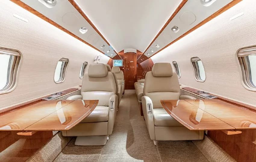 A view of the Challenger 350 cabin with beige leather seats and wood tables.